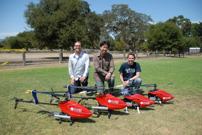 Three men kneeling behind three radio-controlled helicopters outside