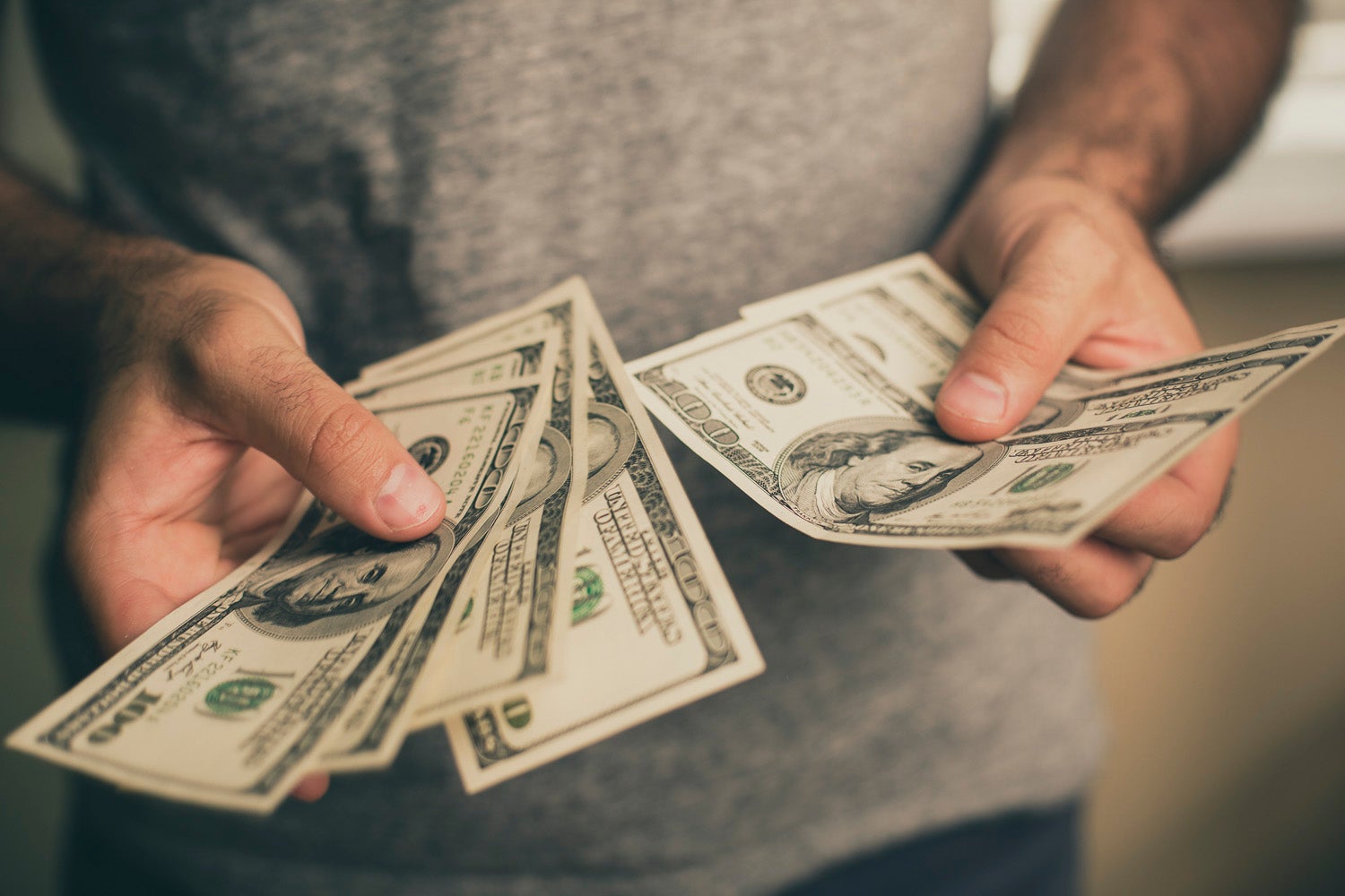A man in a gray T-shirt holds dollars in his hands.