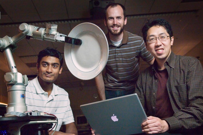 three men posed around a robotic arm holding a plate