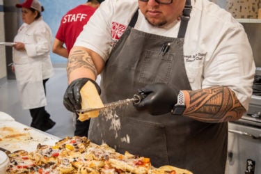 Chef Guinto grating cheese over pizza.