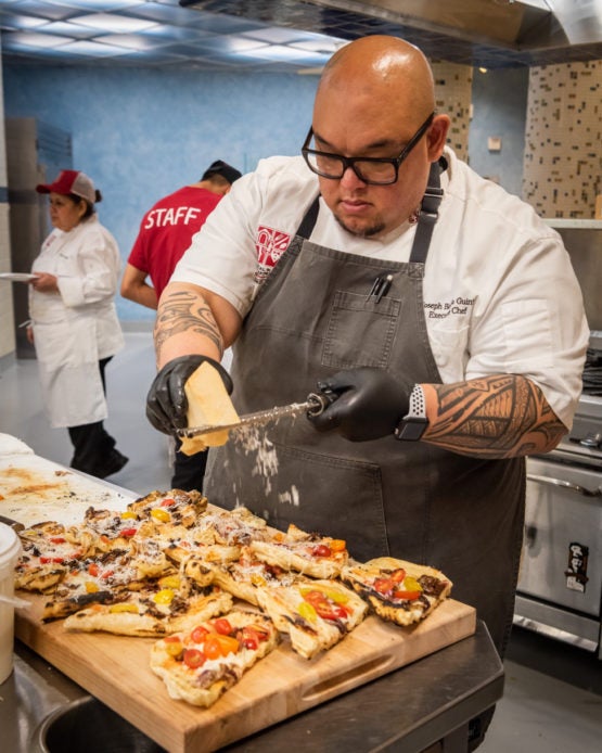 Chef Guinto grating cheese over pizza.