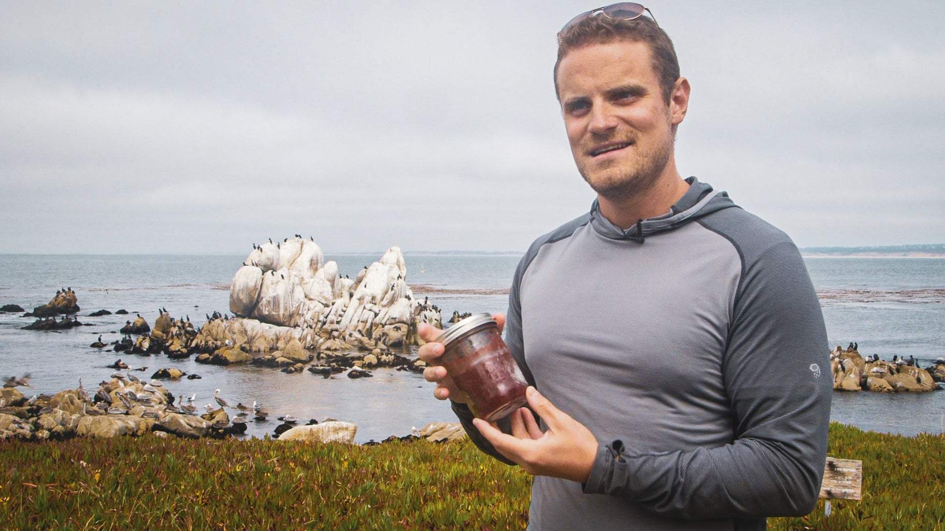 Man standing near beach holding a jar with reddish-pink contents