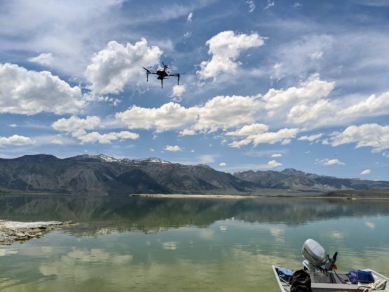 Drone hovers over the water with a mountain range in the background and the back of a motorboat in the foreground