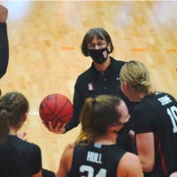 Tara VanDerveer holding a basketball with players around her