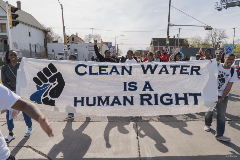 Students walking down a street, holding a banner that says Clean Water is a Human Right