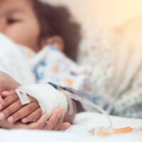 Hand holding child's hand in hospital bed
