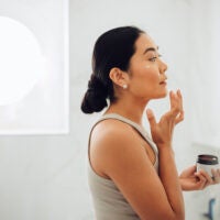 Woman holding face cream and applying it to her cheeks and face.